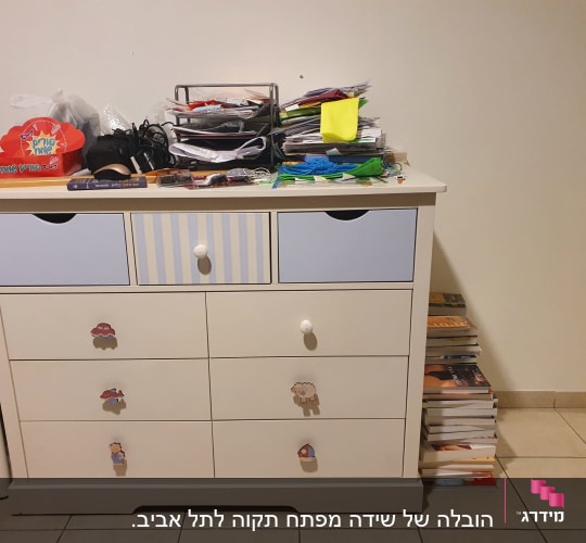 שידה עם מגירות מלאות חפצים וערימת ספרים בצד